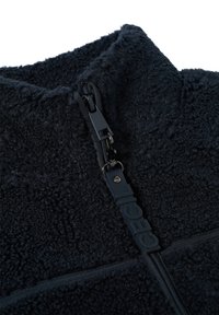 Fleece pulovr v tmavě námořnické barvě s vysokým límcem, s černým zipem a texturovanou tkaninou. Detail loga na táhle zipu.