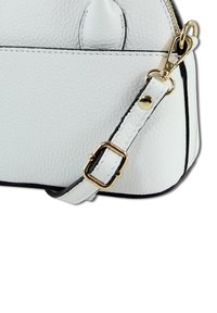 White leather handbag with pebbled texture, gold hardware accents, adjustable strap, and black trim. Close-up view of side and strap.