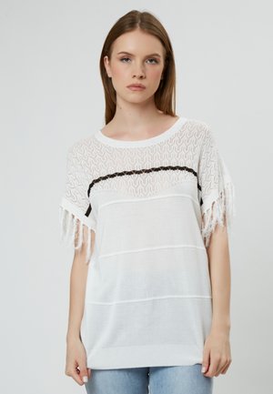 Top bianco lavorato a maglia con un design in pizzo testurizzato, caratterizzato da una striscia orizzontale nera e maniche con frange. Tessuto morbido con una vestibilità morbida.