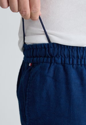 Navyblauwe linnen broek met een elastische tailleband met trekkoord, zijzak en een klein rood, wit en blauw logo accent.