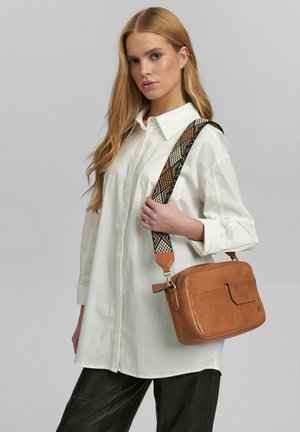 Brun läder crossbody-väska med en mönstrad tygrem med geometriska mönster. Väskan har en rektangulär form och ett framfack.