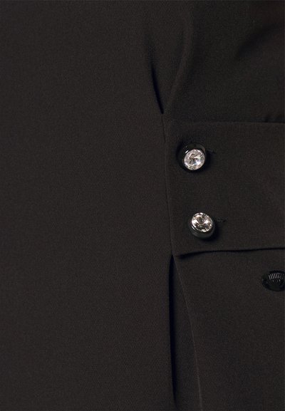 Μαύρος ύφασμα με λεία υφή που διαθέτει τρία γυαλιστερά κουμπιά — δύο στρογγυλές διάφανες πέτρες και μία μαύρη — σε λεπτομέρεια τσέπης.