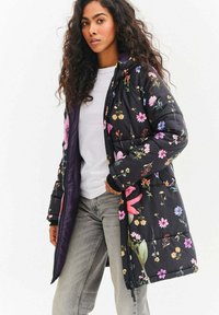 Černý květovaný péřový kabát s mixem růžových, fialových a žlutých květin. Má zip a žebrované manžety. Nositelný přes bílý top.