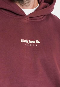 Felpa bordeaux con cappuccio e coulisse, con la scritta "Sixth June Co." e "PARIS" ricamate in rosa chiaro sul petto. Tessuto morbido.