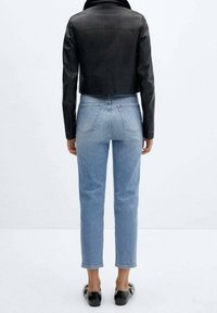 Chaqueta de cuero negra corta sobre jeans de tiro alto en azul claro. Los jeans tienen un corte recto y bolsillos traseros. Unos zapatos planos negros completan el conjunto.