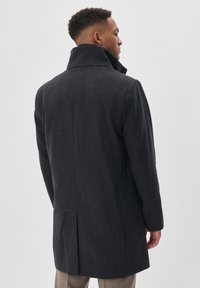 Abrigo de lana gris oscuro con un cuello alto, una abertura en la parte trasera y un corte entallado. La superficie presenta una textura sutil.