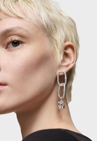 Orecchini in argento con un design a catena collegata, dotati di un ciondolo testurizzato con accenti trasparenti e neri, attaccato a un anello.