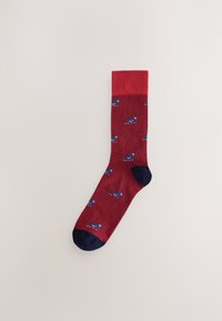 Chaussette rouge en maille texturée, ornée de petits motifs d'animaux bleus. Le bord-côte est d'un rouge uni, tandis que le bout et le talon sont bleu marine.