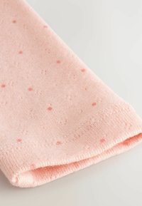 Weicher rosa Strickstoff mit kleinen, subtilen dunkleren rosa Punkten und einem sauberen Stich entlang der umgeschlagenen Kante.