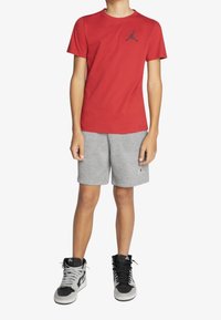 Czerwony bawełniany T-shirt z czarnym logo Jordana, w połączeniu z szarymi szortami z logo oraz czarno-szarymi wysokimi trampkami. Prosty sportowy design.