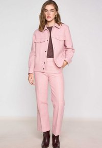 Veste en laine mélangée rose pâle avec deux poches poitrine et un col, associée à un pantalon rose pâle assorti et des bottes à cheville marron foncé.