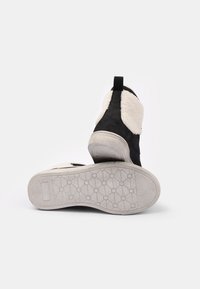 Svarta mocka stövlar med vita fårskinnsdetaljer och en texturerad grå gummisula. Bakhändig för enkel påtagning.
