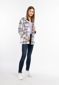 Geruite flanellen jack in wit, paars en grijs, met knopen en twee zakken, gedragen over een lichtpaars topje, gecombineerd met donkere jeans en witte sneakers.