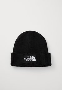 Svart stickad mössa med vikbar muddkant, med en rektangulär logotypapplikation som visar "The North Face" i vitt på en svart bakgrund.