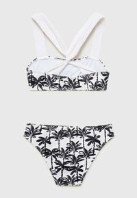 Černobílé plavky s potiskem, které obsahují top na ramínka se zkříženými popruhy a designem palmových listů, doplněné o odpovídající nízké bikiny.