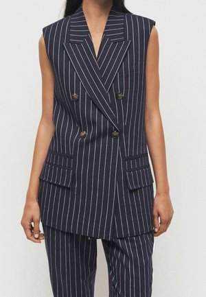 Sleeveless navy blazer with white pinstripes, double-breasted buttons, flap pockets, worn with matching pinstripe trousers.