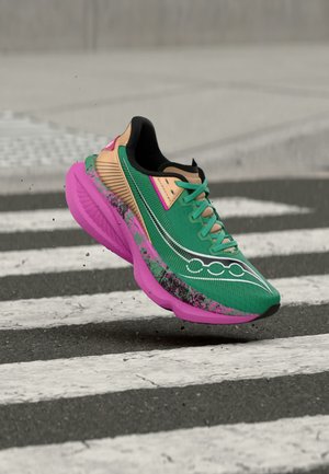 Pantof de alergare verde și bej cu talpă roz cu pete, suspendat deasupra asfaltului cu dungi albe de trecere pentru pietoni.