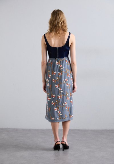 Jean και φόρεμα με λουλούδια, με εφαρμοστό, σκούρο μπλε μπούστο και ημιδιαφανές γκρι φούστα με πορτοκαλί και λευκή κεντημένη λουλούδια.