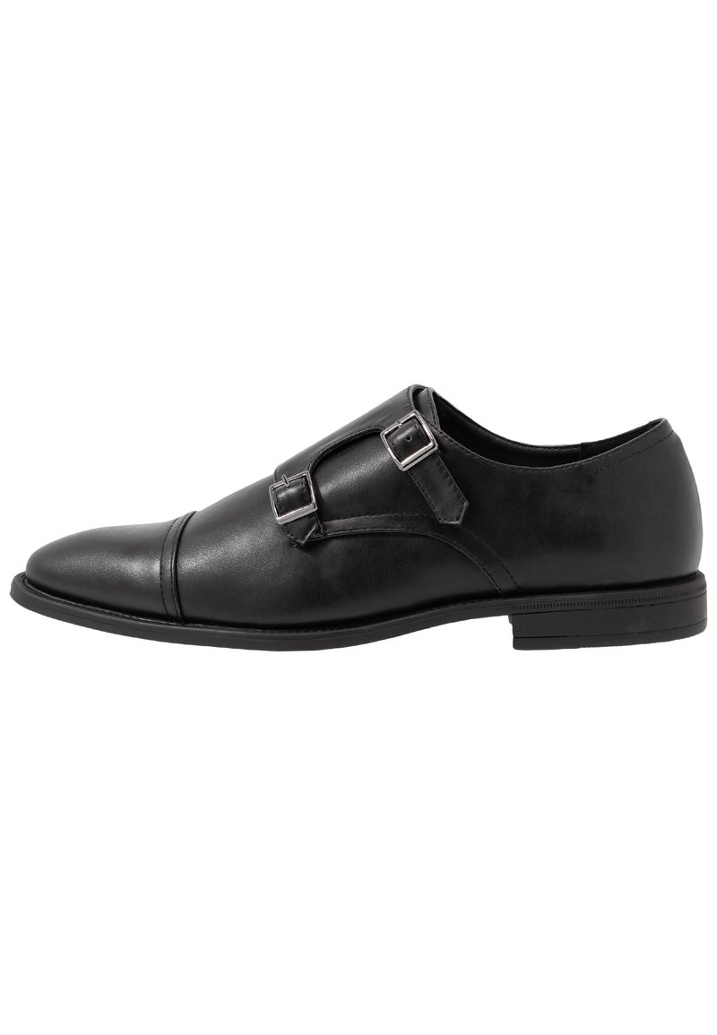 Chaussure monk strap en cuir noir avec deux boucles en argent, design à bout capteur, bout rond et semelle en caoutchouc de profil bas. Texture lisse, silhouette élégante.