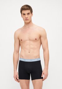 Čierne boxerky s elastickým pásom svetlo modrej farby s nápisom "HUGO". Hladká, elastická tkanina poskytuje pohodlie a dobré prispôsobenie.