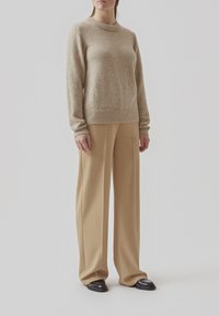 Beige uldtrøje med rund halsudskæring og ribbede manchetter, parret med lys beige bukser med vidde og sorte sko.