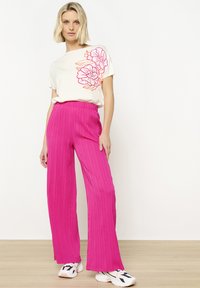 Witte katoenen t-shirt met roze bloemenborduursels, gecombineerd met wijd-uitlopende, gestructureerde roze broeken en witte sneakers. Eenvoudige, casual outfit.