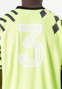 Zöld sportmez, amelyen egy nagy fehér 3-as szám található, fekete díszcsíkokkal a vállakon és strukturált anyagból készült. Fekete gallér részletezéssel.
