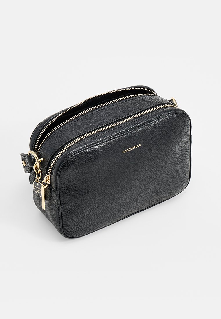 Sac à main en cuir noir avec une finition texturée, fermetures à glissière doubles et quincaillerie dorée. Présente un nom de marque en relief sur le devant.