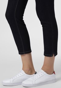 Vita lädersneakers med rund tå och gummisula. Har svarta och röda detaljer på hälen. Bärs med mörka jeans som når anklarna.