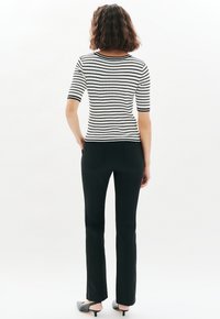 Top de rayas en blanco y negro con canalé y mangas cortas, combinado con pantalones rectos negros y zapatos de tacón negros, visto desde atrás.