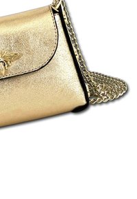 Gouden metallic schoudertas met een klepsluiting, voorzien van een bij-embleem en een zilveren schakelriem. Soepele textuur met contrasterende zwarte randen.