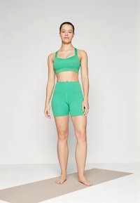 Completo activewear verde che include un reggiseno sportivo aderente e pantaloncini a vita alta, realizzati in tessuto liscio ed elastico. Progettato per offrire comfort e libertà di movimento.