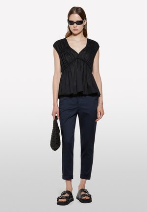 Haut noir à encolure en V sans manches avec un détail de tissu froncé, associé à un pantalon slim-fit bleu marine, des sandales noires et un sac à main noir texturé.