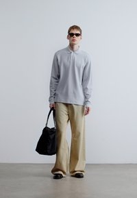 Ανοιχτό γκρι πόλο με μακριά μανίκια, εκρού παντελόνι φαρδιάς γραμμής, μαύρη τσάντα και γυαλιά ηλίου. Λείο ύφασμα με διακριτικές λεπτομέρειες υφής.