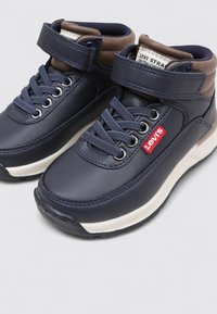 Botines azul marino con parte superior sintética lisa, cierre de cordones y tira de velcro, suela crema y una pequeña etiqueta roja de Levi's en el lateral.