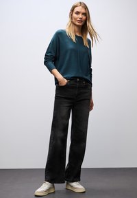Turkusowy, oversize sweter z długimi rękawami, zestawiony z szerokimi, czarnymi dżinsami i kremowymi sneakersami. Gładka tekstura, casualowy krój.