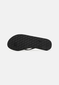 Semelle de tongs noire avec un motif en diamant texturé et deux indentations circulaires. Le matériau en caoutchouc offre de la flexibilité. Design minimaliste.