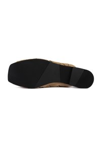 Semelle de chaussure en suède beige avec un fond en caoutchouc noir texturé, présentant des rainures horizontales et une forme distincte pour une meilleure traction et stabilité.