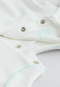 Witte katoenen romper met zilveren drukknoopjes en lichtblauwe stiksel langs de halslijn. Label met verzorgingsinstructies zichtbaar aan de binnenkant.