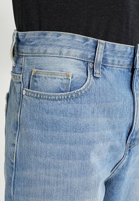 Ljusblå denimjeans med rak skärning, med en framficka, synlig sömnad och knäppning i midjan.