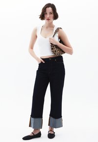Jeans in denim scuro con gamba ampia e orlo unico, caratterizzato da pannelli in denim chiaro e dettagli con frange. Abbinati a una canotta bianca e una borsa con stampa animale.