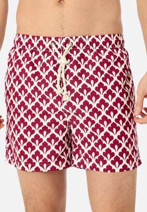 Herren-Badeshorts mit einem abstrakten floralen Muster in Burgunderrot und Weiß sowie einem weißen Kordelzugbund, getragen von einer stehenden Person.