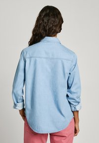 Lichtblauwe denim overhemdd met lange mouwen, knoopmanchetten en een gebogen zoom. De achterkant heeft een eenvoudige ontwerp met schoudernaden en een kraag.