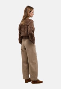 Pull en maille texturée marron avec un design cropped, associé à un pantalon beige à jambes larges et des chaussures en daim marron. Vue arrière décontractée.