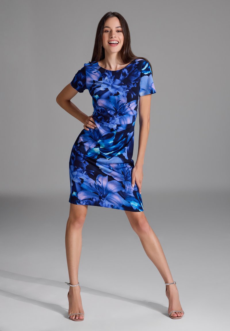 Robe à imprimé floral dans des nuances de bleu et de violet, manches courtes, design ajusté, longueur genou, texture de tissu lisse et légère brillance.