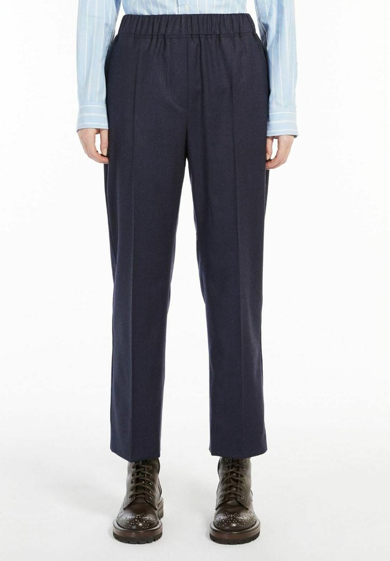 Personne portant un pantalon bleu marine à taille élastique, une chemise à rayures bleu clair à manches longues et des bottines à lacets marron foncé.