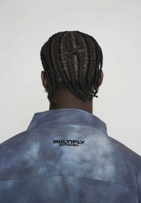 Modrá tričko s batikou a golierom, na zadnej strane s čiernou vyšívanou značkou "MULTIPLY APPAREL". Tkanina vyzerá hladko s jemným leskom.