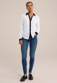 Balta garām piedurknēm pogājama krekla ar melnu apkakli un aprocēm, apvienota ar ziliem šaurajiem džinsiem un melniem kurpju zābakiem. Gluda auduma tekstūra.