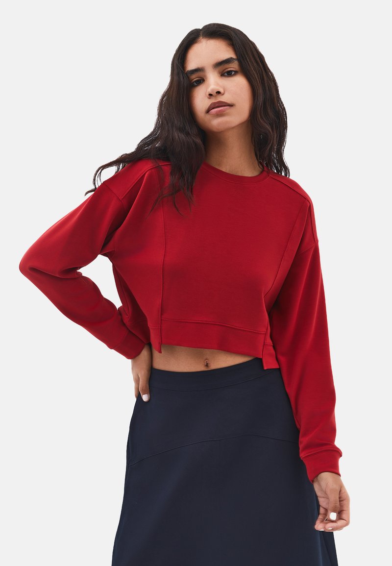 Felpa rossa corta con maniche lunghe, colletto a coste e morbido al tatto, abbinata a una gonna blu navy, che mostra un look casual e confortevole.