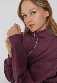 Felpa viola con zip e colletto alto, con polsini a coste. Presenta una zip in metallo e una vestibilità comoda. Tessuto morbido e liscio.